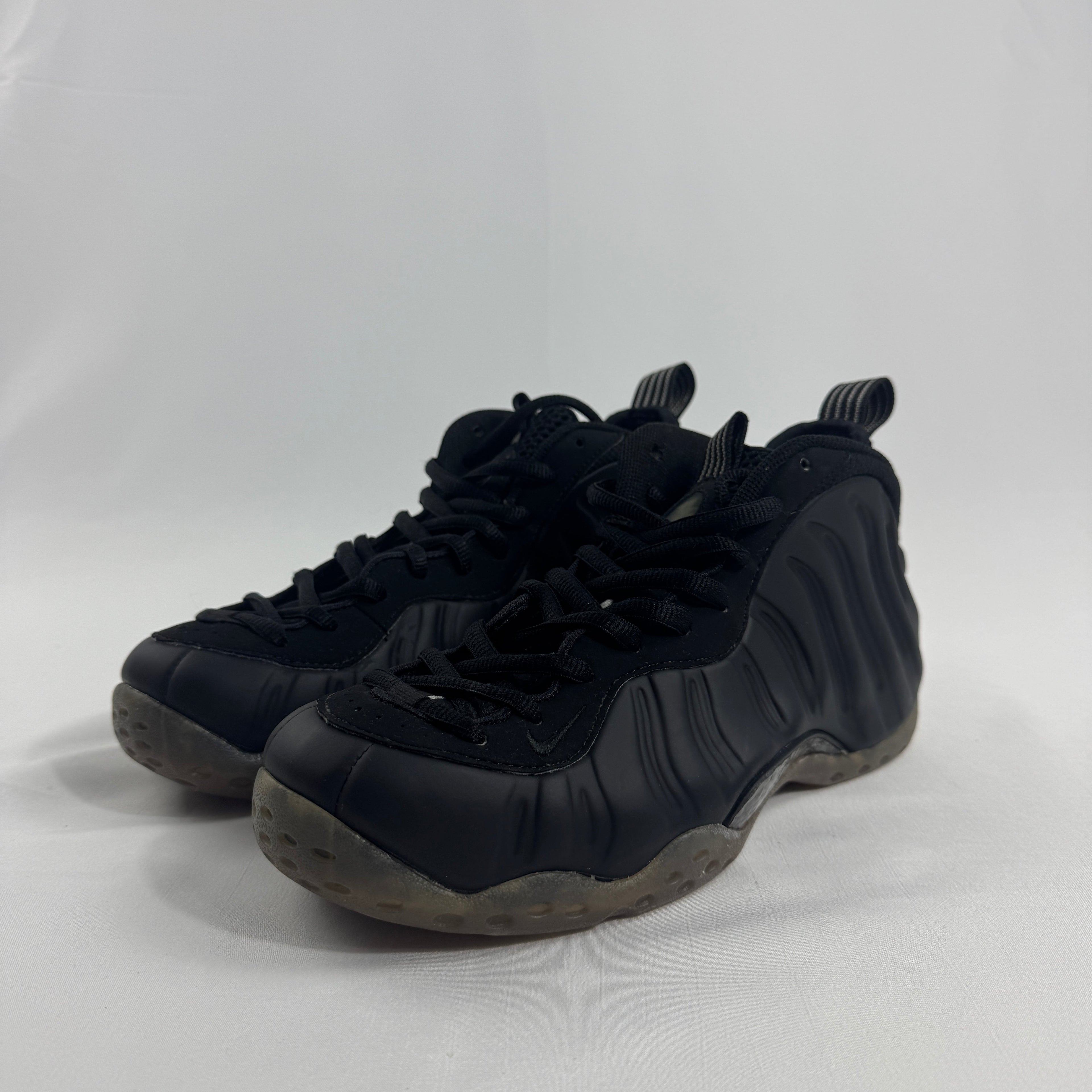 Black Nike trainers with textured sides, thick rubber soles and black laces, displayed against a plain white background.