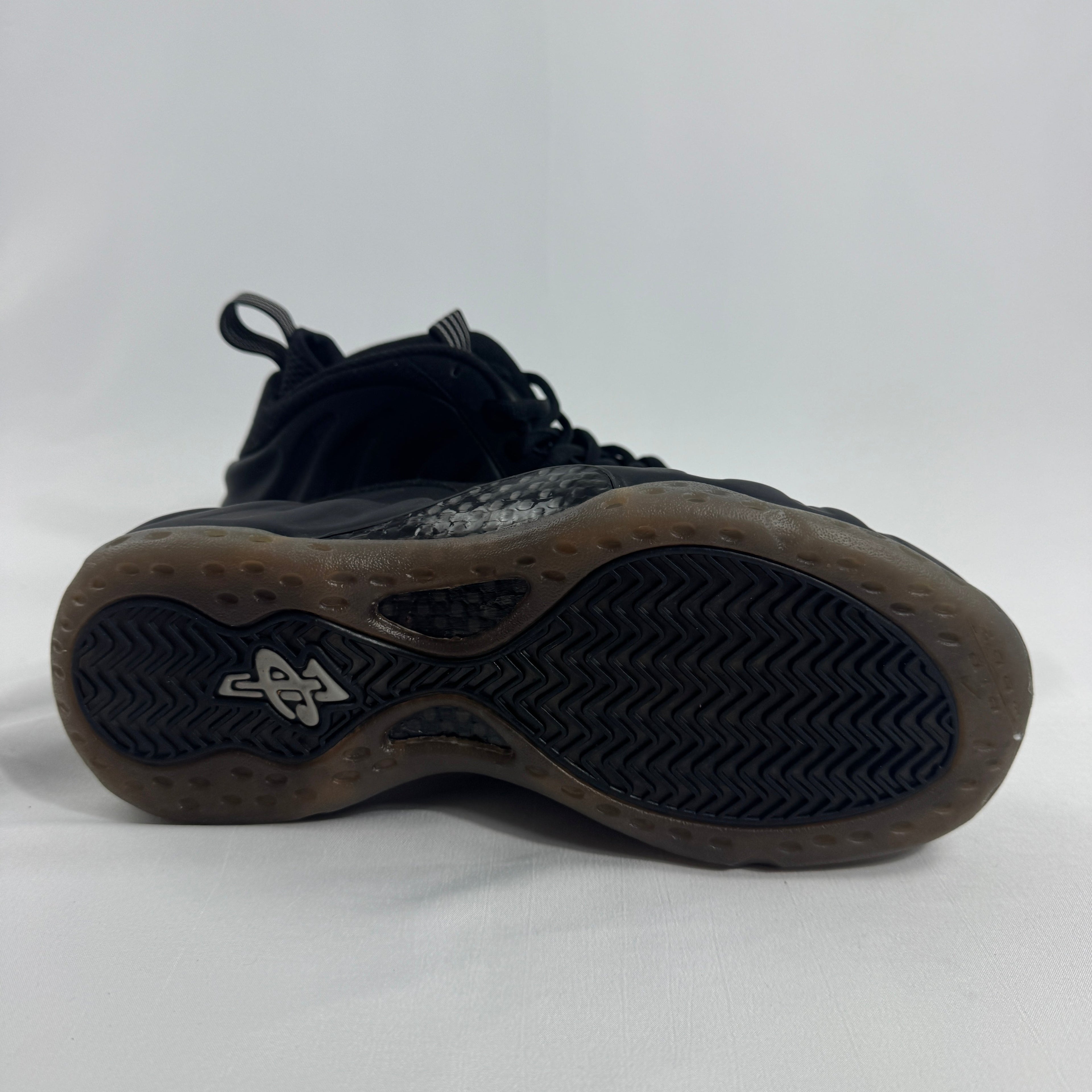 Black Nike basketball trainer on its side, showing a wavy textured sole and small white logo by the heel on a plain white background.