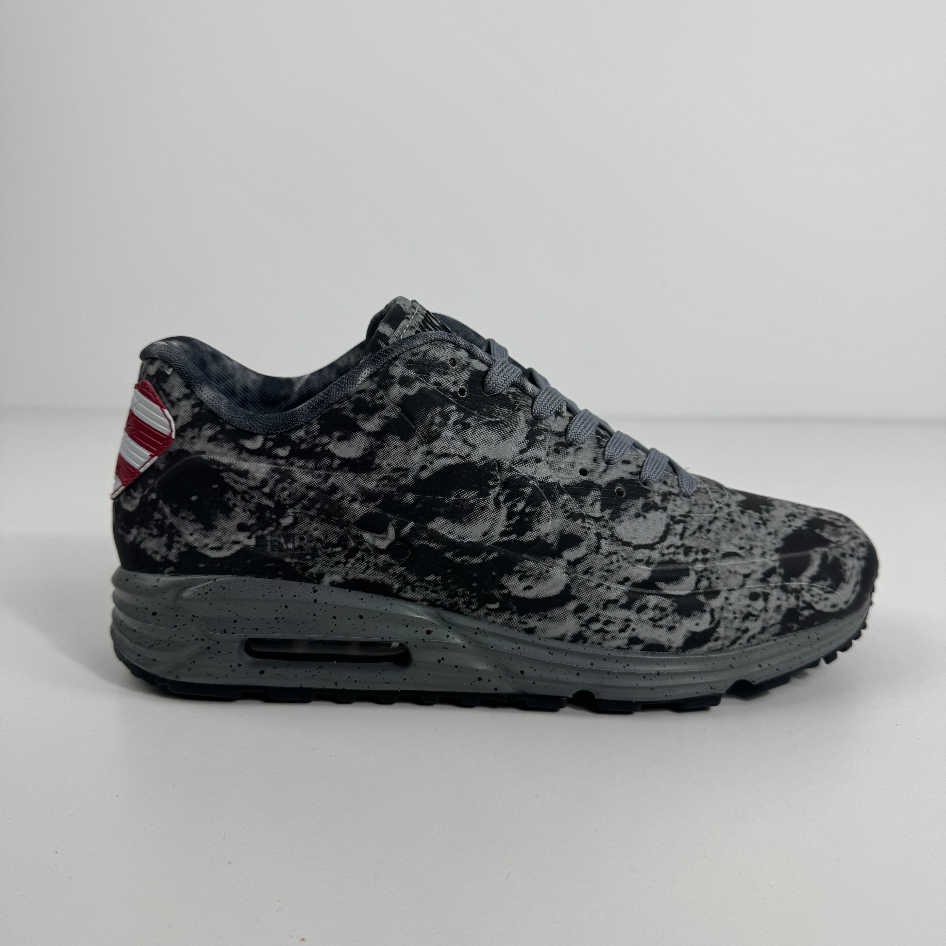 Nike trainer in grey with a moon-like textured upper, grey laces, Lunarlon sole and a small American flag on the heel.