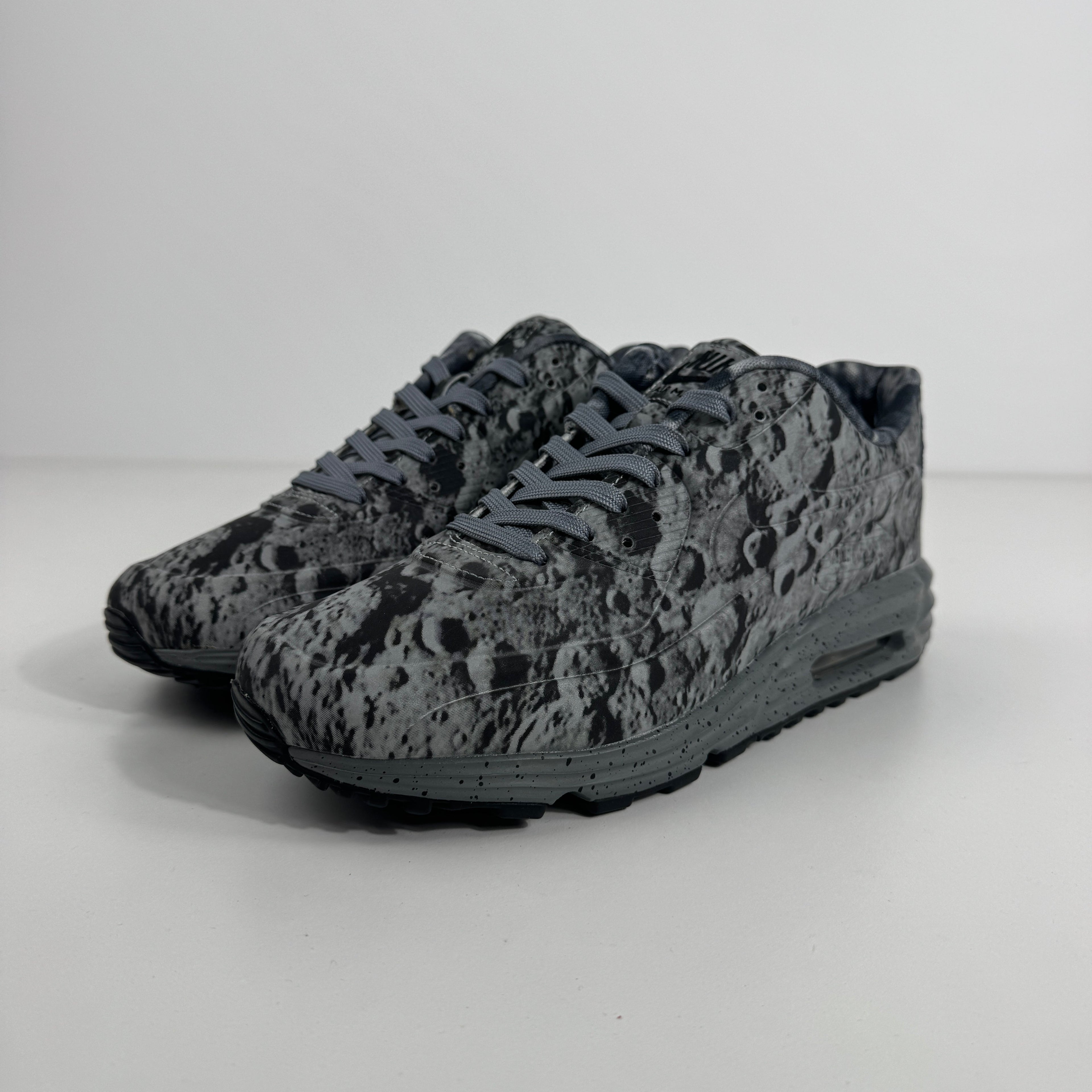 Nike Air Max Lunar90 SP trainers in grey and black with crater-like patterns, displayed on a plain white background.