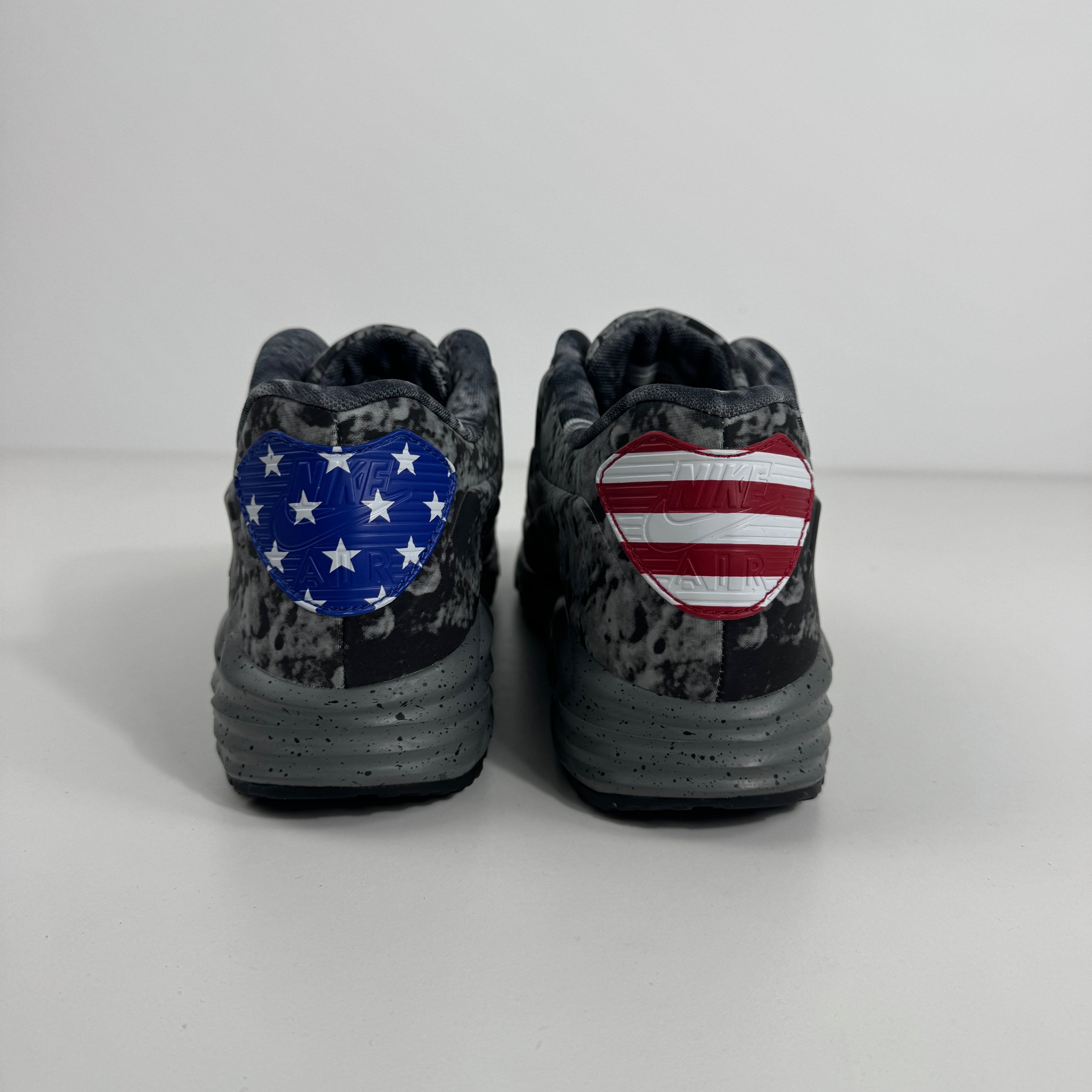 Black and grey Nike Air Max Lunar90 SP trainers seen from behind, featuring hearts with American flag motifs on each heel.