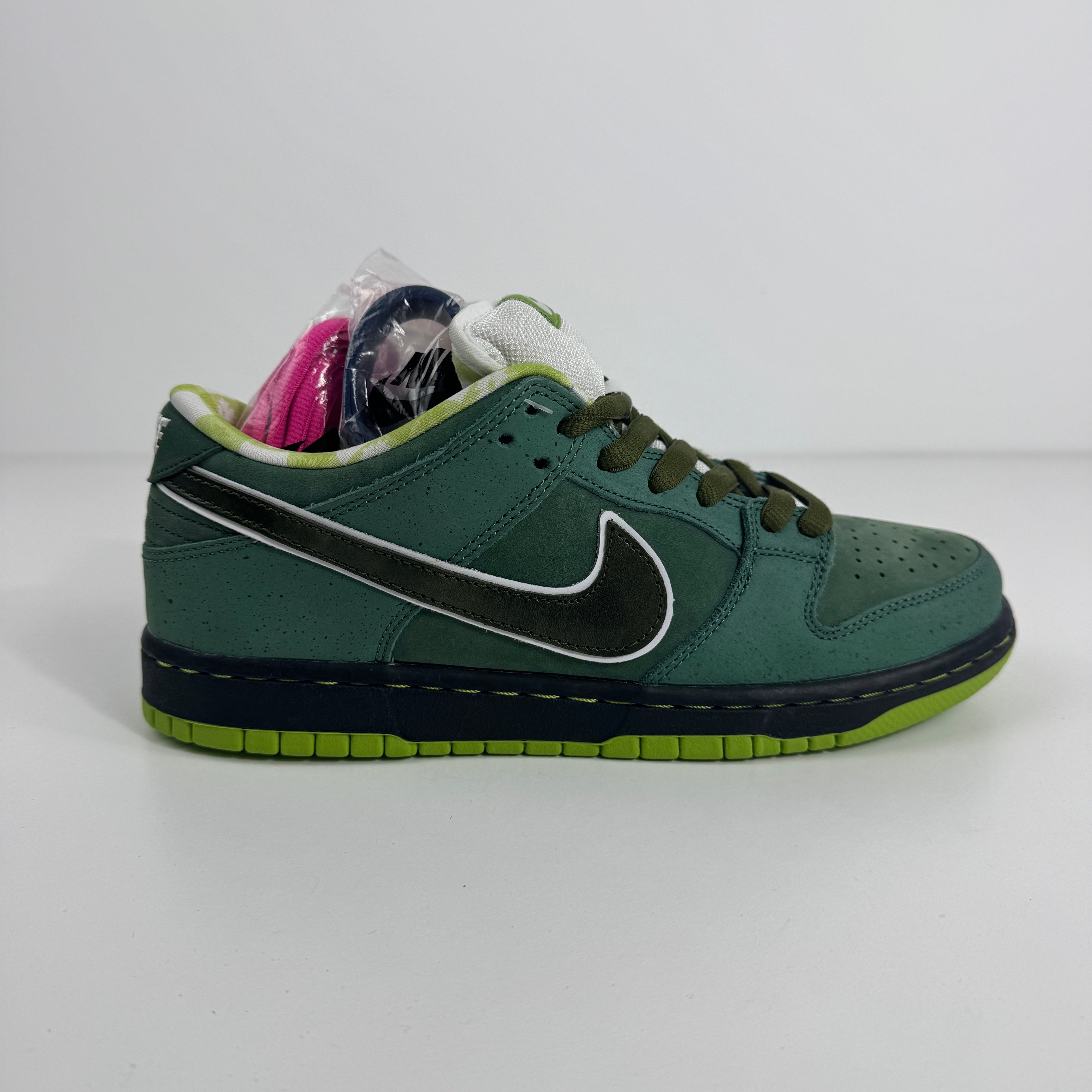 Nike SB Dunk Low trainer with a green upper, black swoosh, lime green sole, and white tongue on a white background.