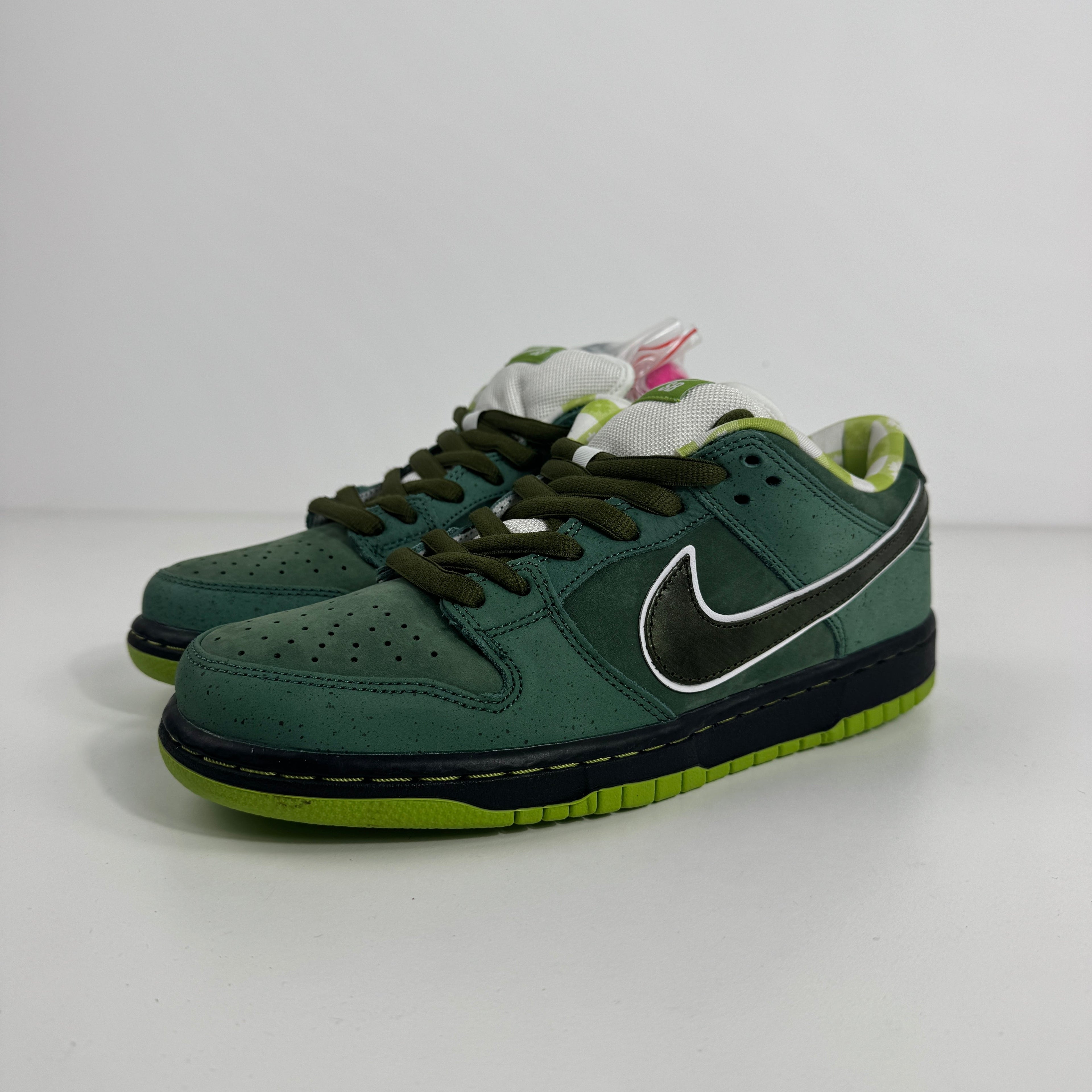 Nike SB Dunk Low Pro trainers in green with black laces, white and black swoosh, white tongue and green-checked lining on a white surface.