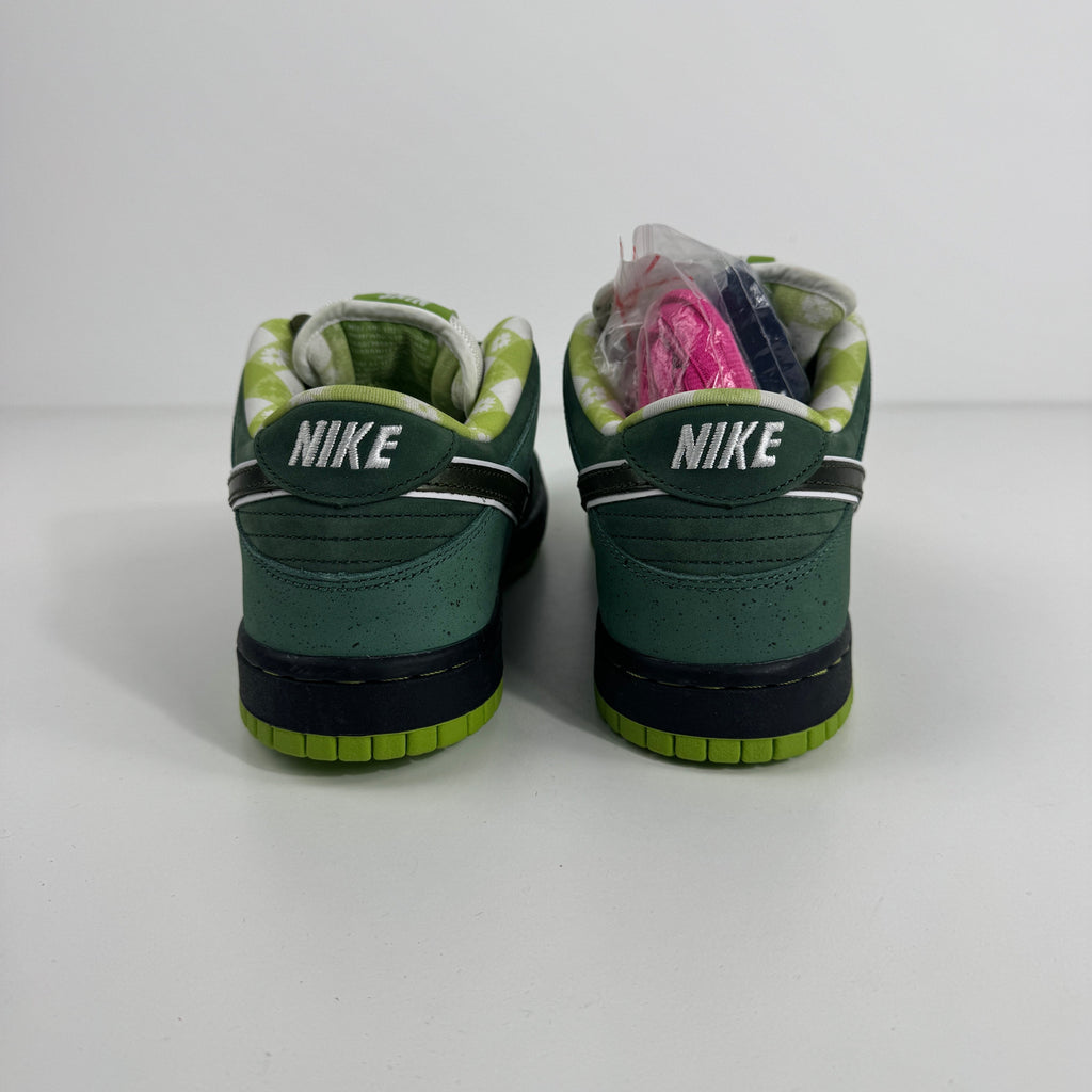 Green Nike SB Dunk Low sneakers viewed from the back, with a checkered lining and extra pink and purple laces on the left shoe.