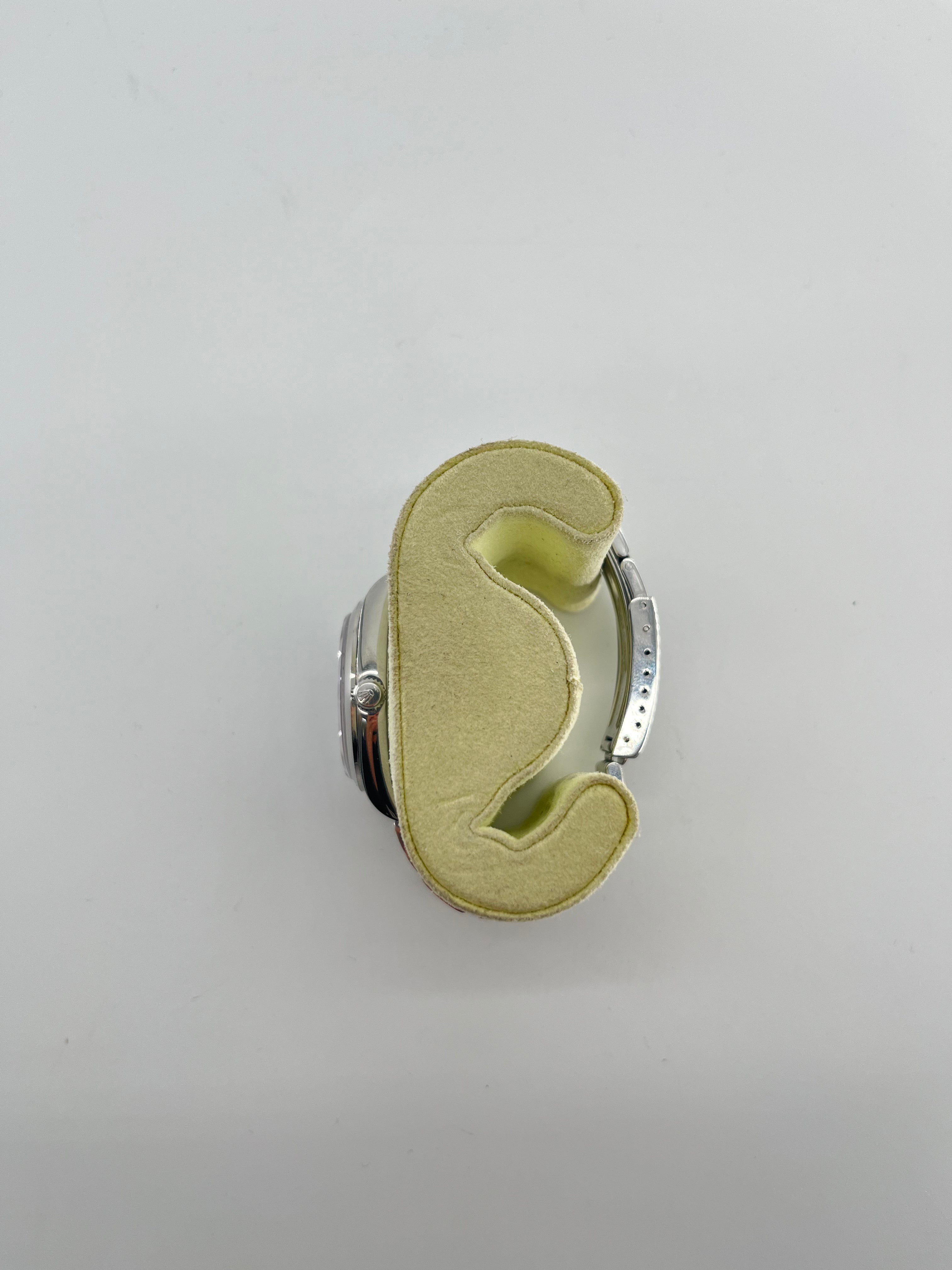 A Rolex Air-King watch with a stainless steel case is shown from above on a light yellow foam holder against a white background.