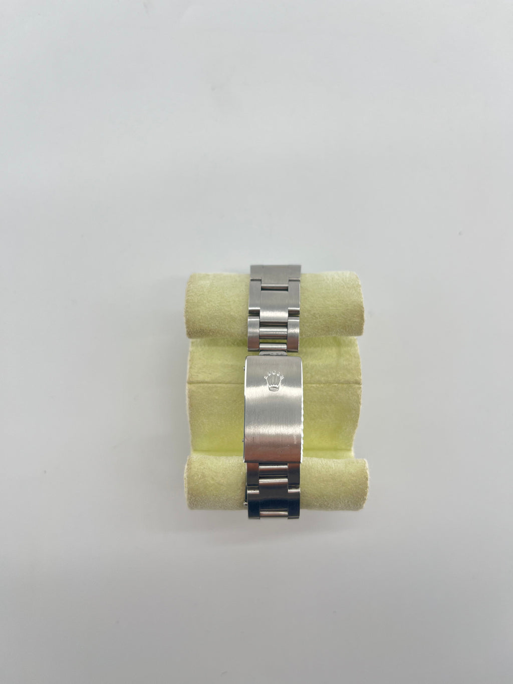 Silver metal Rolex bracelet with clasp and crown logo, shown on pale yellow foam against a plain white background.