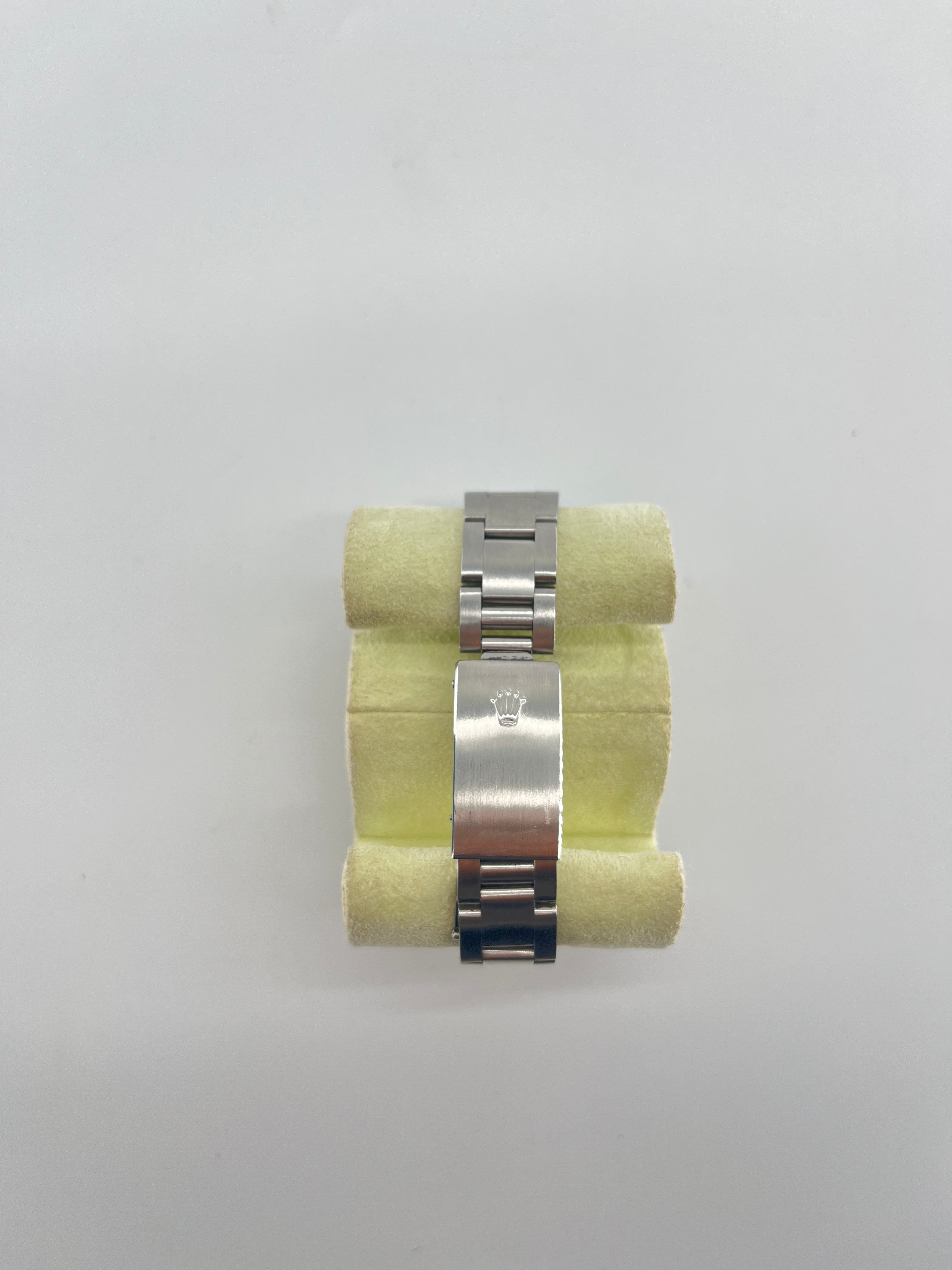 Silver metal Rolex bracelet with clasp and crown logo, shown on pale yellow foam against a plain white background.