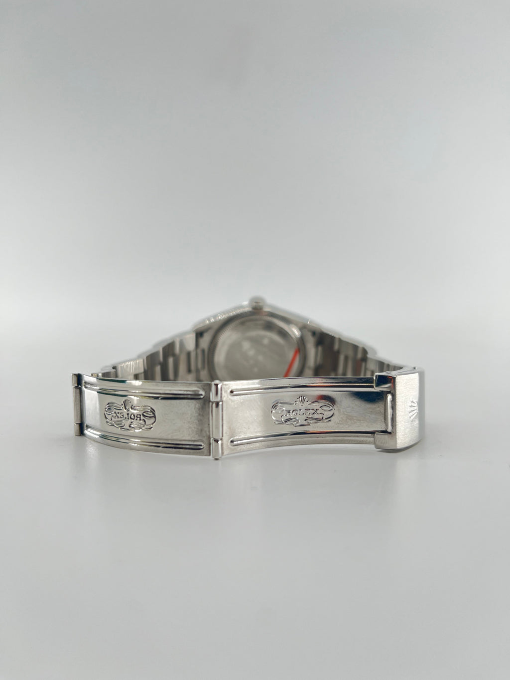 A silver Rolex wristwatch with a metal bracelet is displayed open, showing the engraved clasp and interior details on a light background.