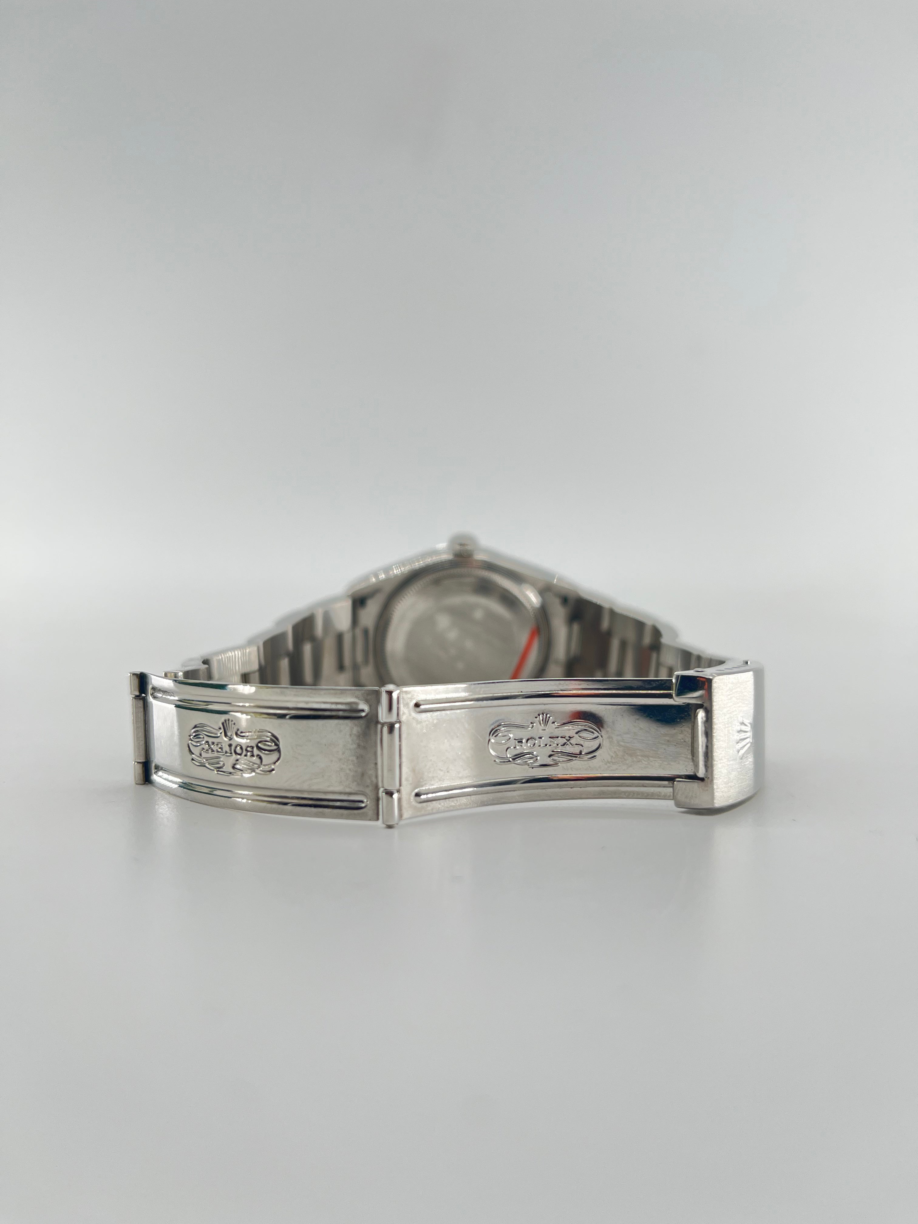 A silver Rolex wristwatch with a metal bracelet is displayed open, showing the engraved clasp and interior details on a light background.