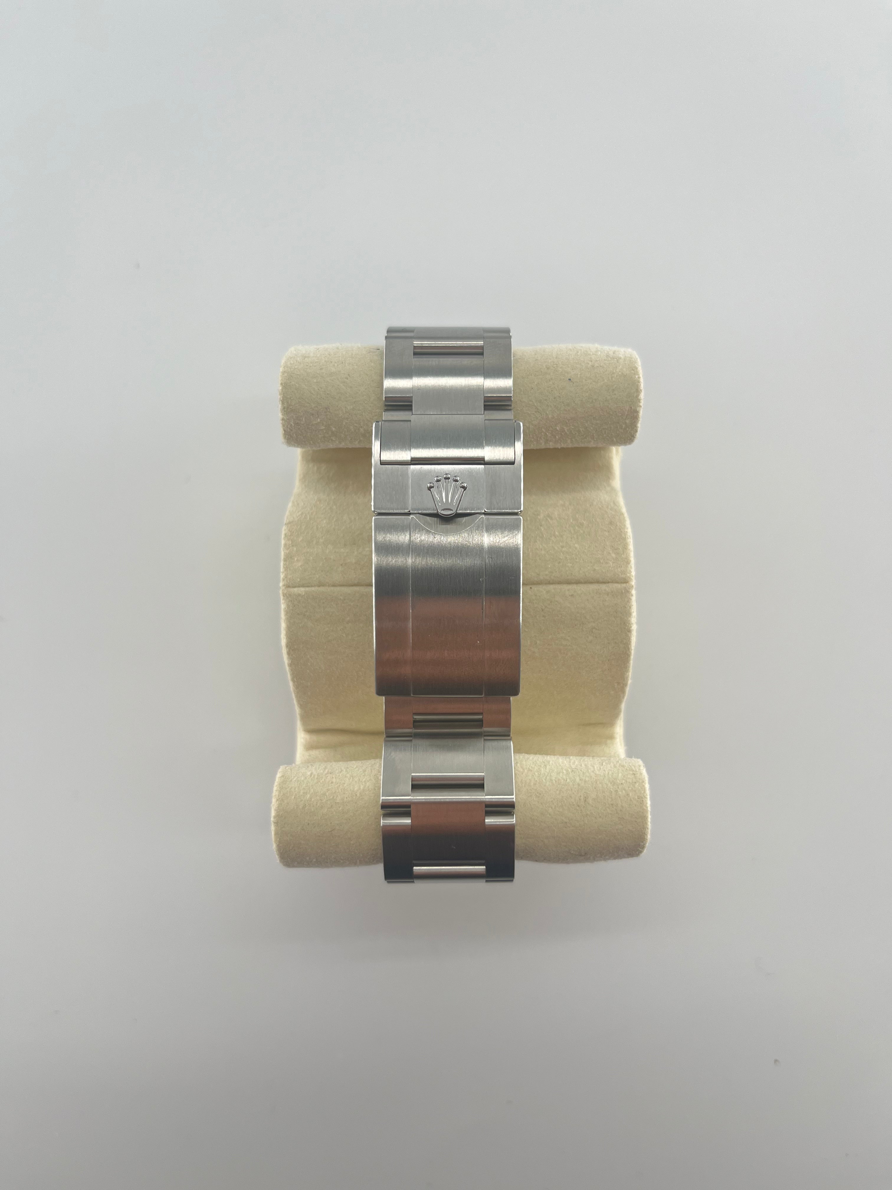 Rolex watch with a stainless steel bracelet and folding clasp, displayed on a beige padded holder against a white background.