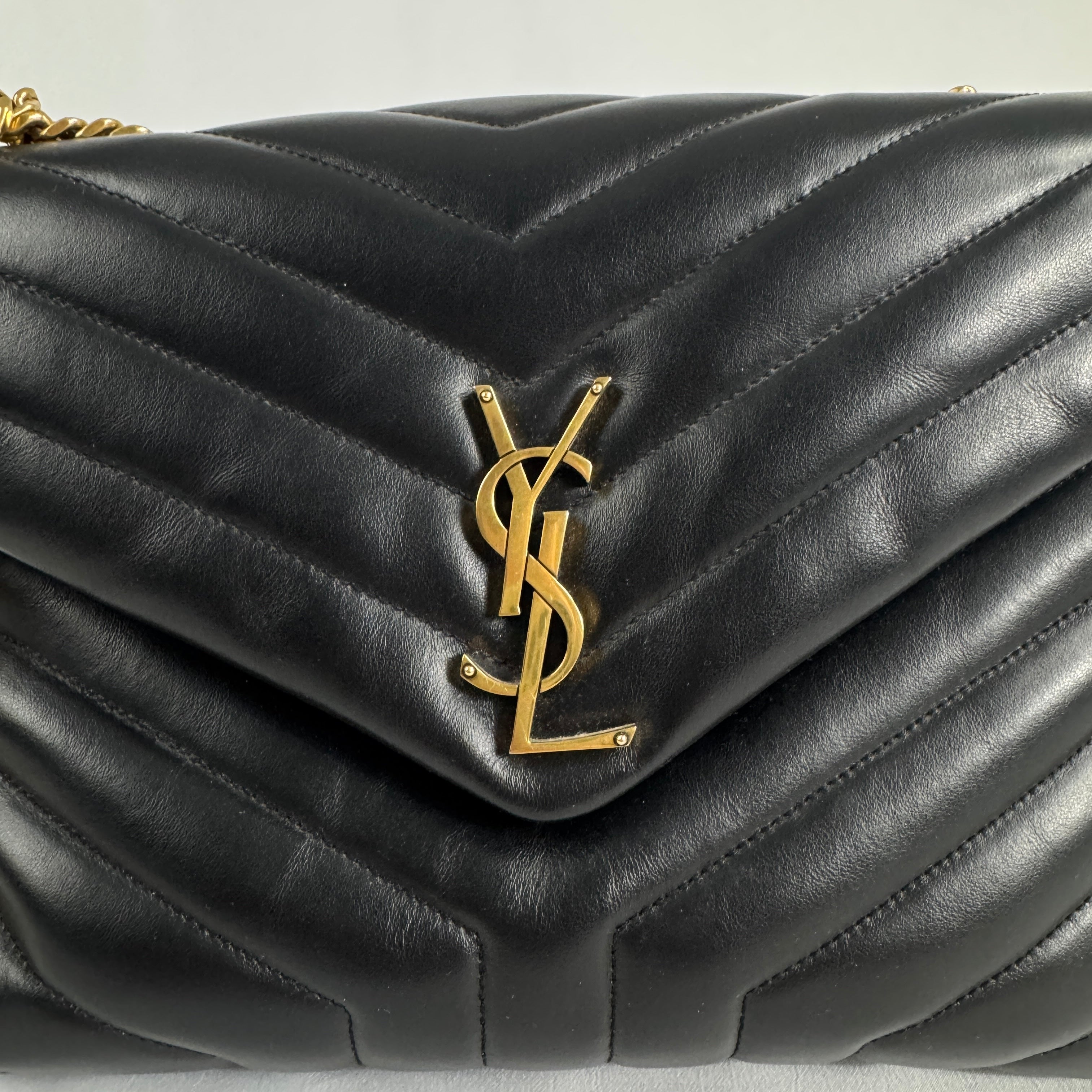 The Saint Laurent LouLou Crossbody Bag is a quilted leather handbag featuring the signature YSL logo, a chain strap, and a