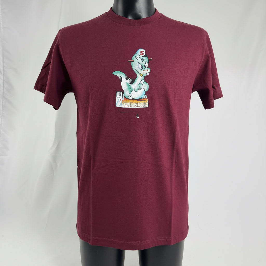 The Supreme Dinosaur Shirt is a cotton T-shirt featuring a dinosaur-themed graphic, often presented in a bold, playful