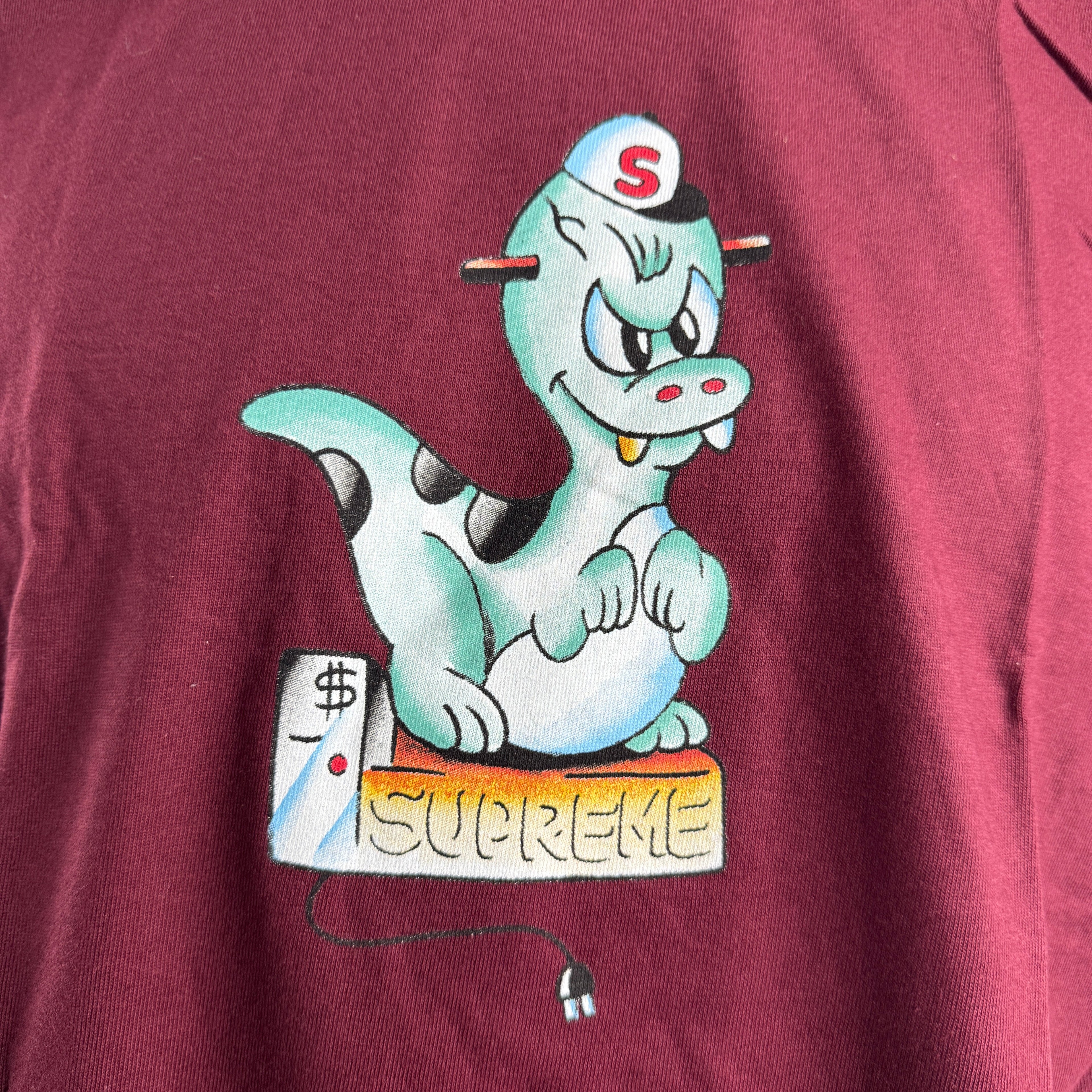 The Supreme Dinosaur Shirt is a cotton T-shirt featuring a dinosaur-themed graphic, often presented in a bold, playful