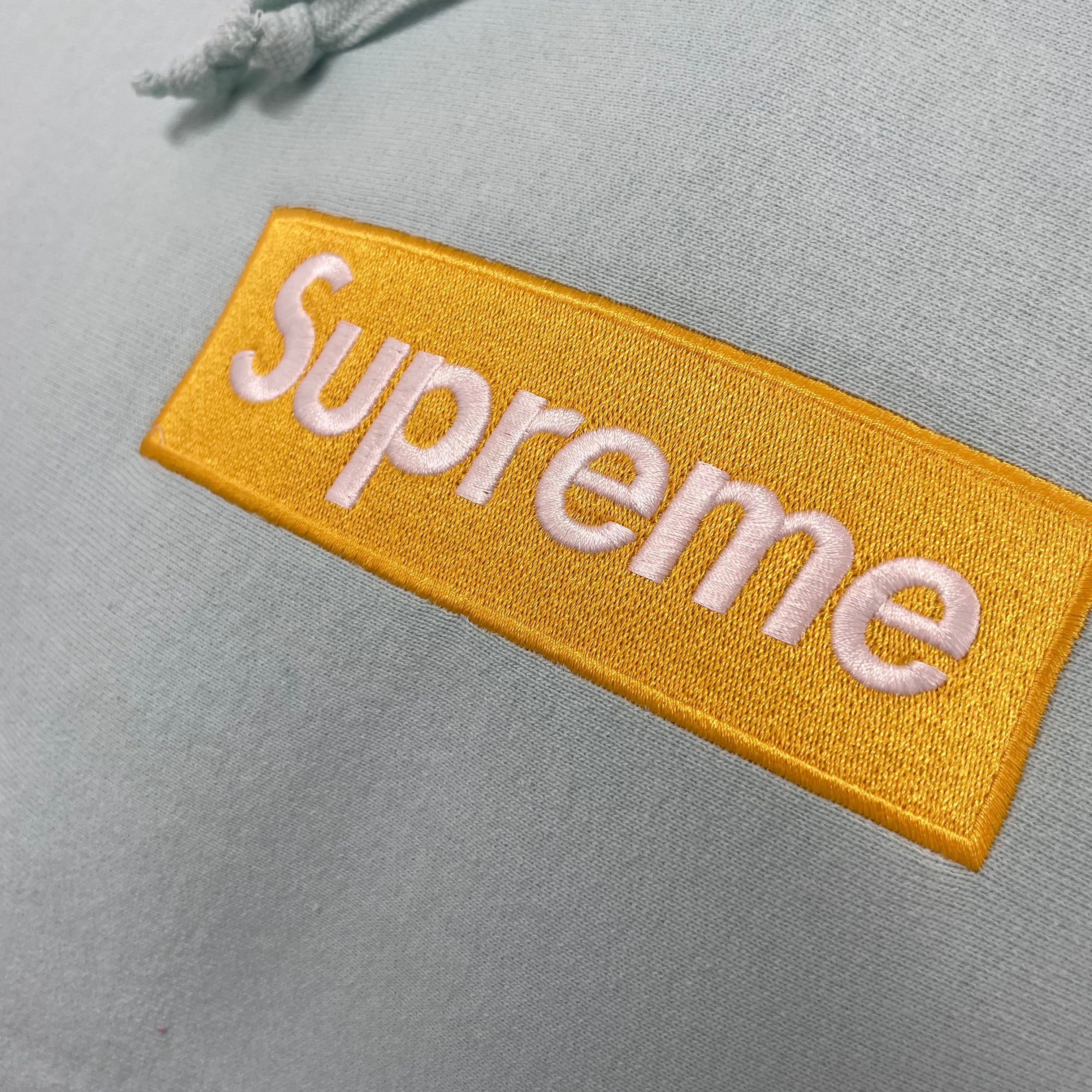 The Supreme Gold Box Logo Hoodie Ice Blue is a heavyweight cotton hoodie featuring the iconic Supreme Box Logo embroidered