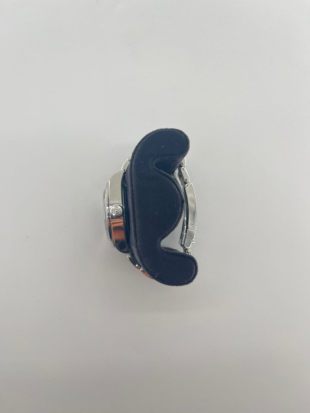 A silver Tudor wristwatch with a black dial rests on a curved black cushion, photographed from above against a plain white background.