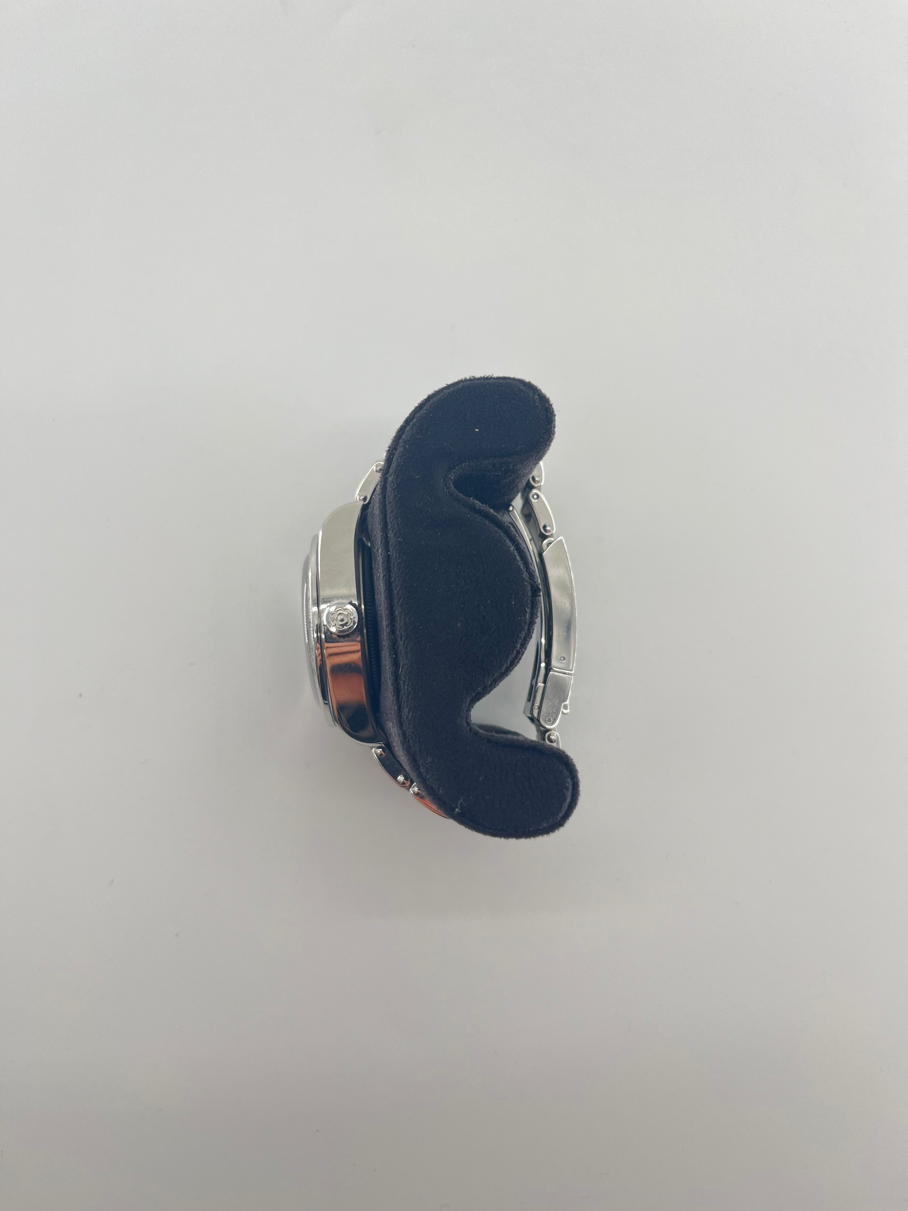 A silver Tudor wristwatch with a black dial rests on a curved black cushion, photographed from above against a plain white background.