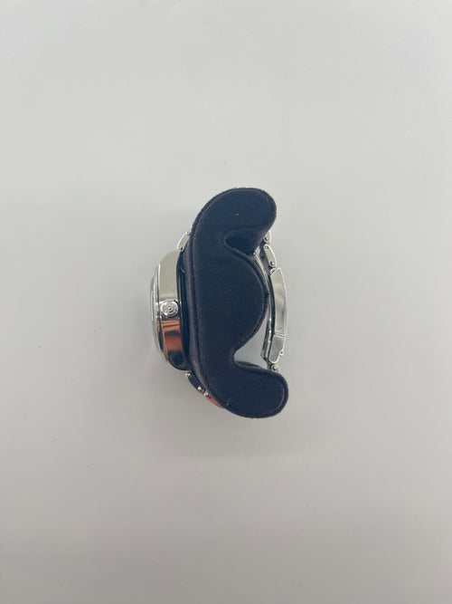 A silver Tudor wristwatch with a black dial rests on a curved black cushion, photographed from above against a plain white background.