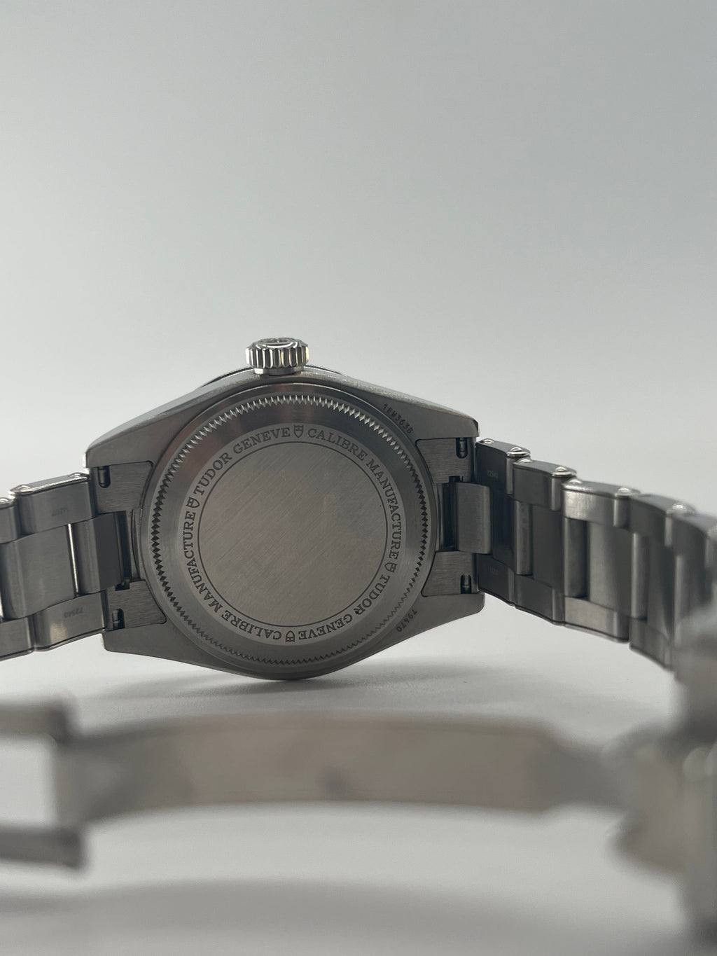Rear view of a TUDOR wristwatch showing the engraved case back and open metal bracelet against a plain white background.