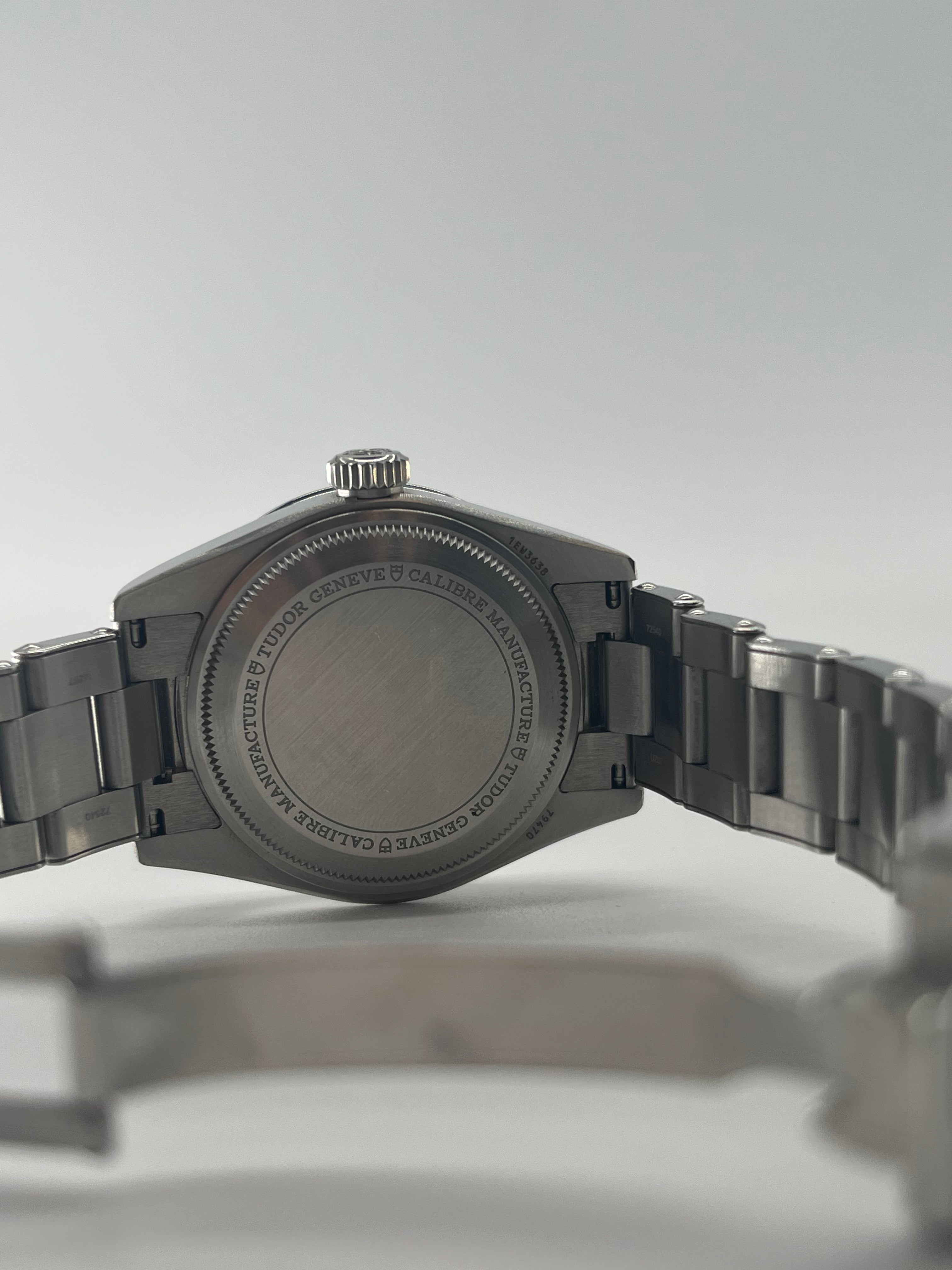 Rear view of a TUDOR wristwatch showing the engraved case back and open metal bracelet against a plain white background.