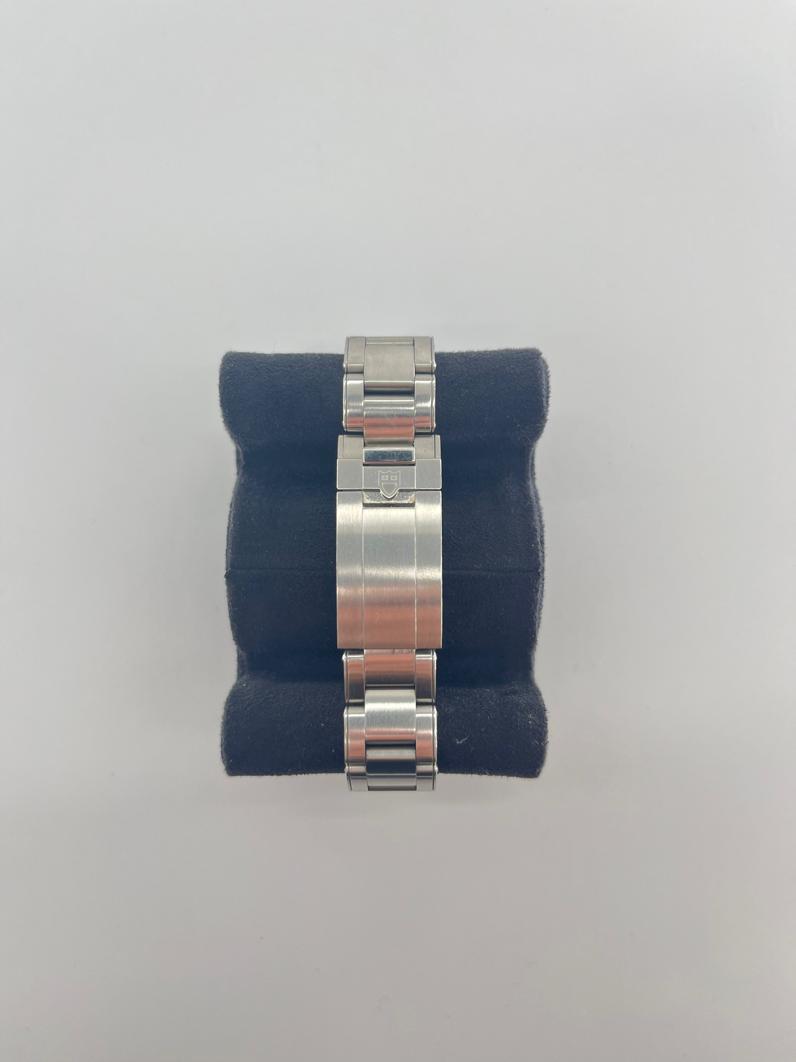 Stainless steel TUDOR wristwatch band with clasp, displayed on a black velvet cushion against a white background.