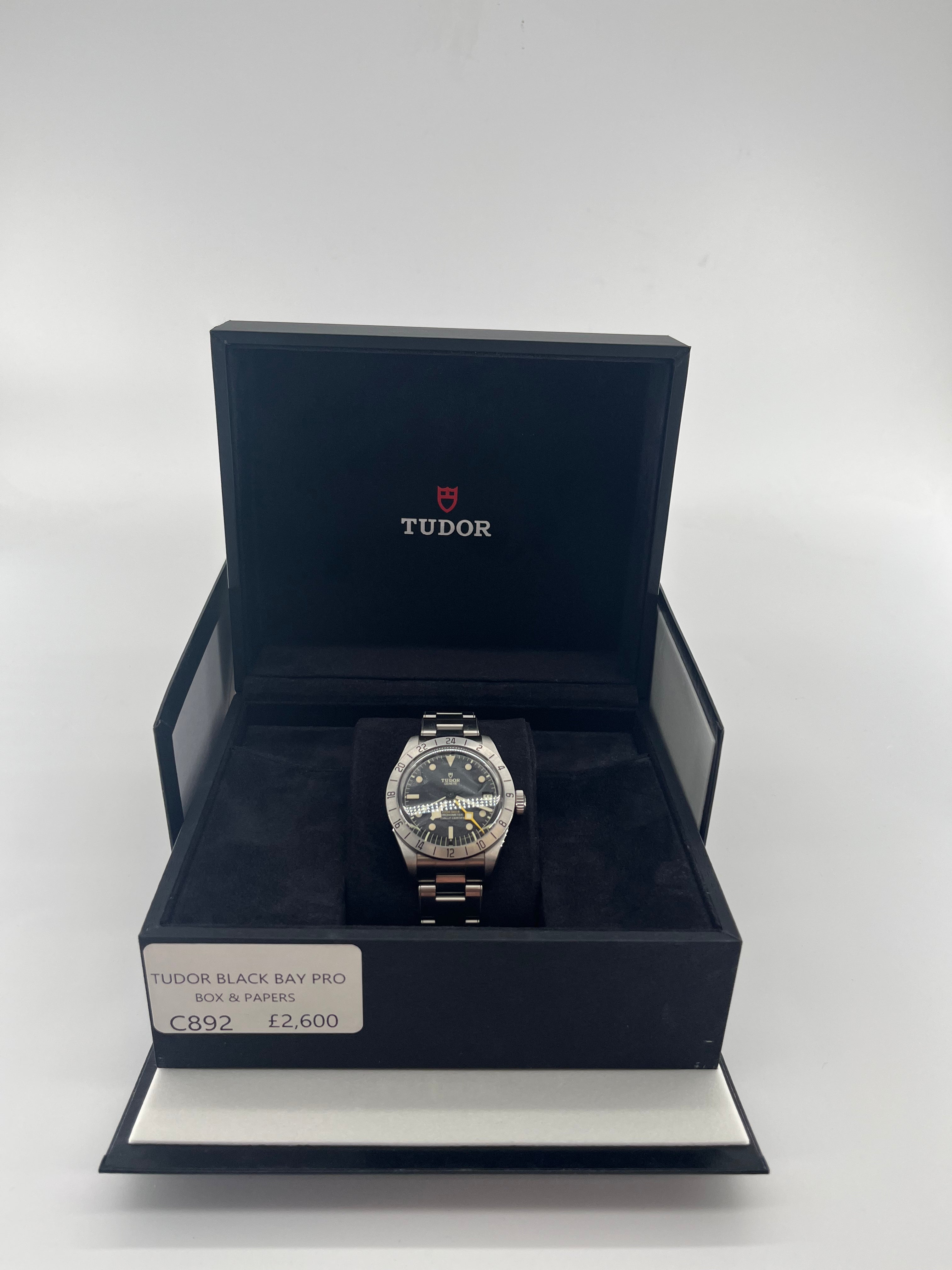 TUDOR Black Bay Pro wristwatch with a black dial on a bracelet in an open branded box, price tag £2,600, on a white background.