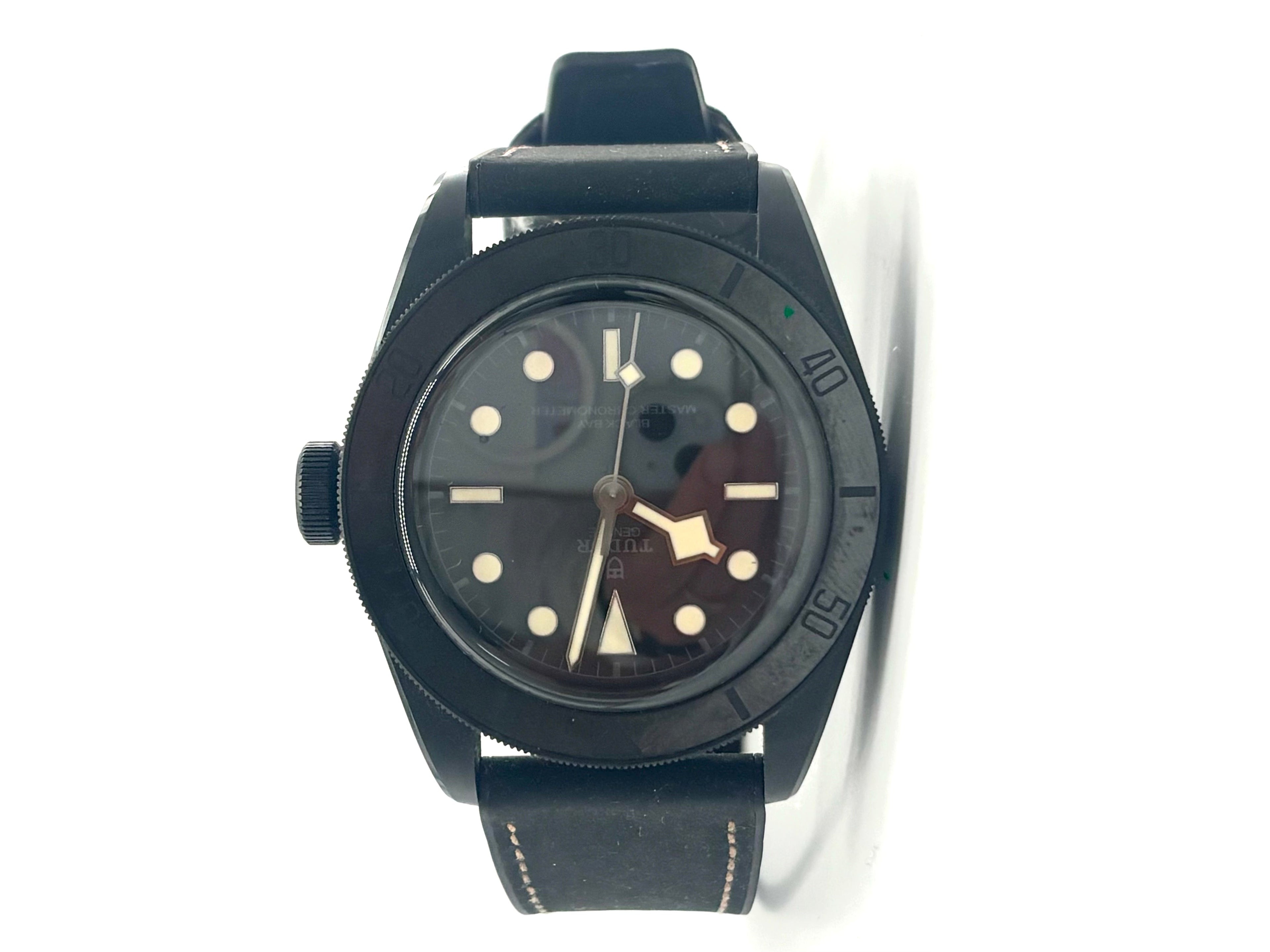 TUDOR ceramic black wristwatch with a round face, white hour markers, large hands and black leather strap with white stitching.