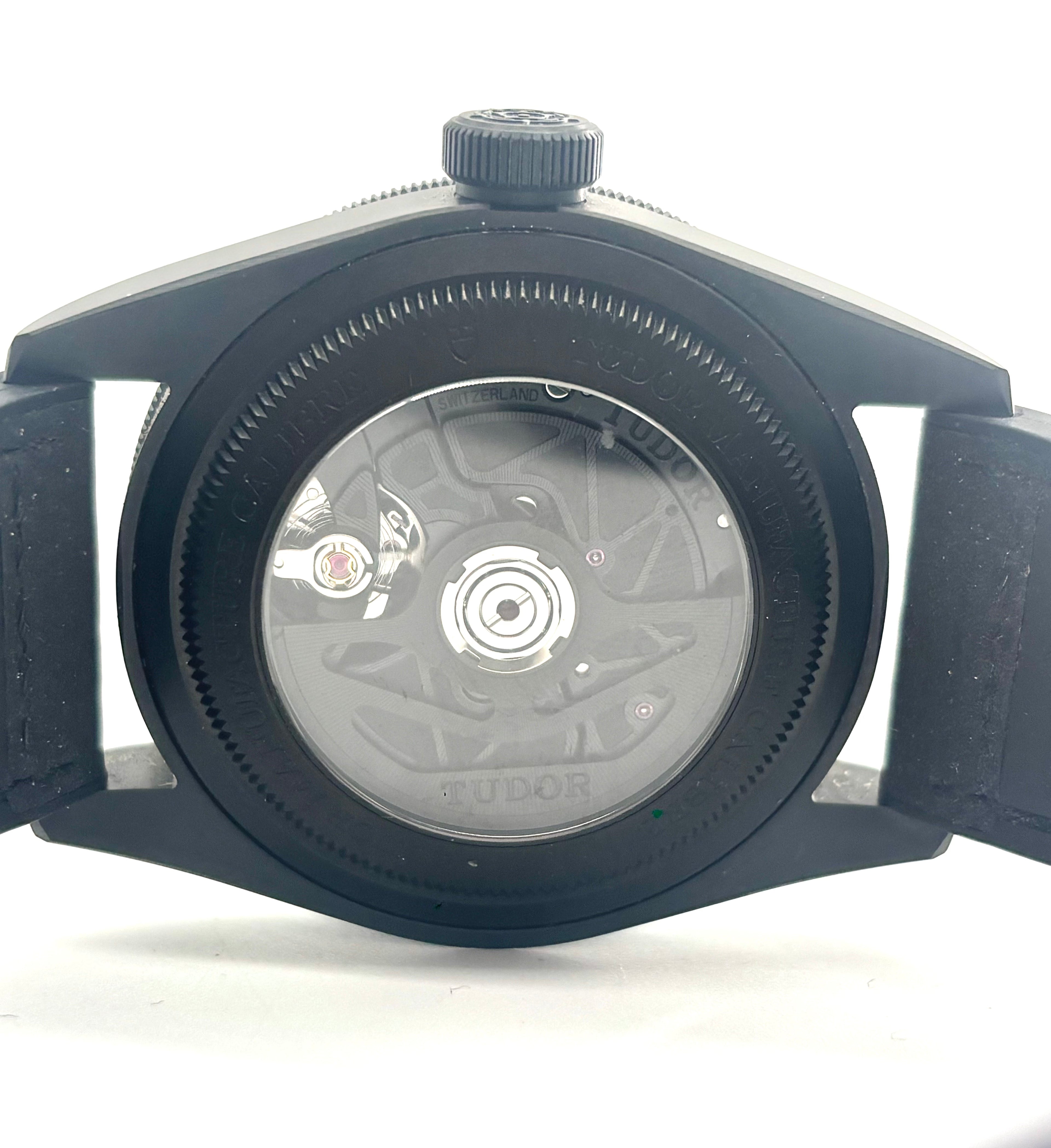 TUDOR wristwatch with a visible automatic movement through a clear case back, black strap, and textured crown.