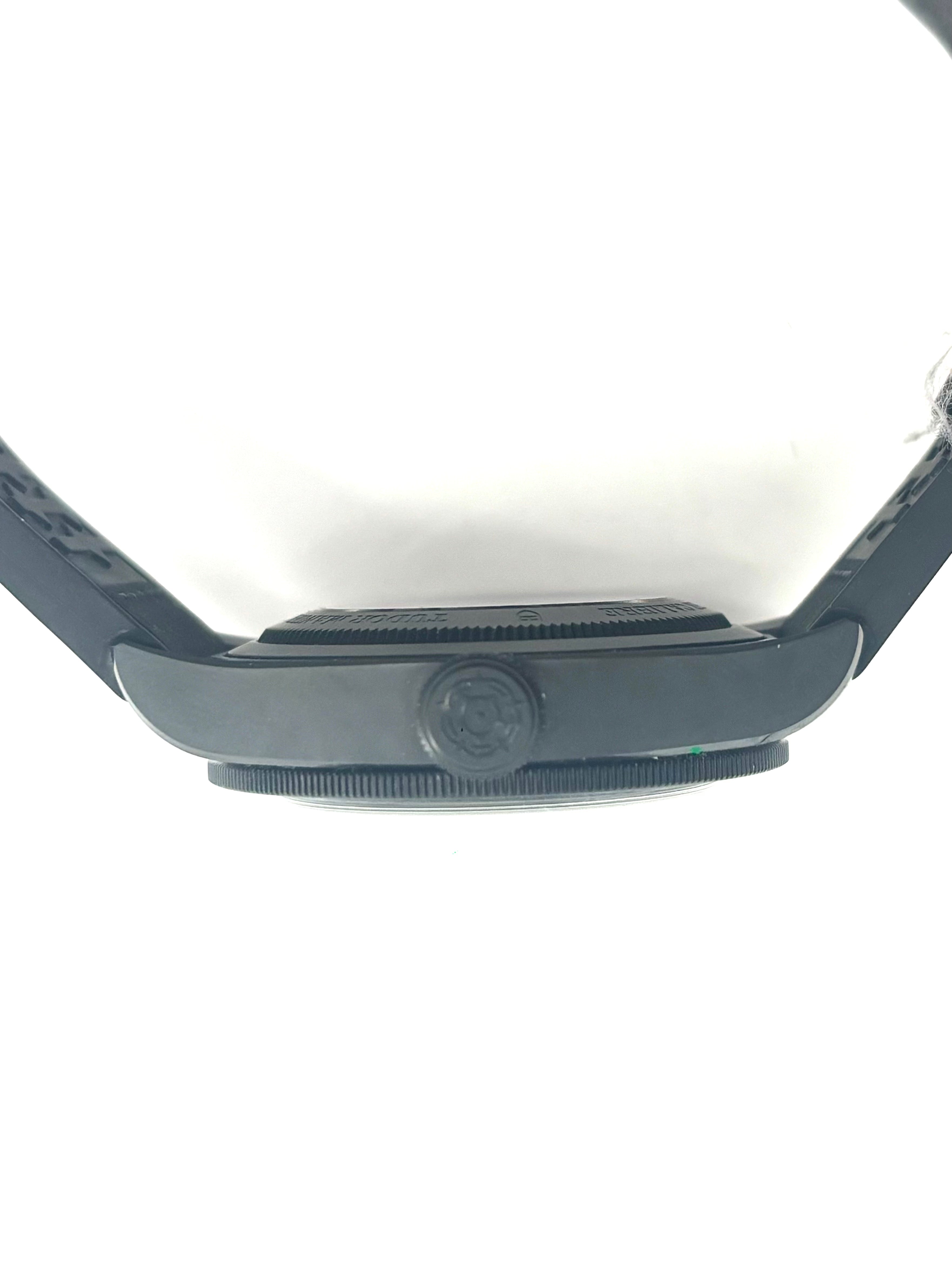 Side view of a black Tudor ceramic wristwatch with an embossed crown logo on the crown and part of the strap, set against white.